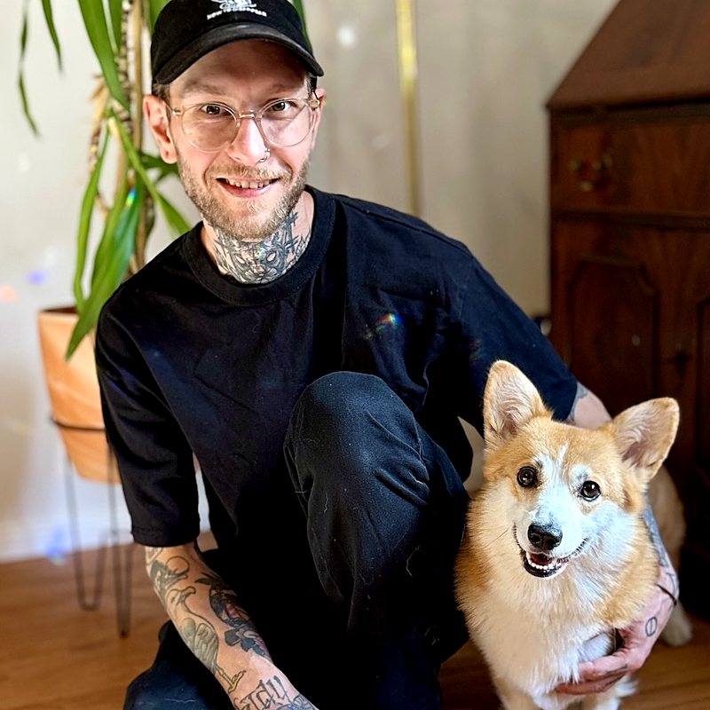 Matthias Lindl kniet auf einem Holzboden neben seiner Hündin Holly, einem Corgi